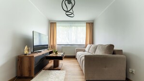 En moderne stue med sofa, fjernsyn, træskab og en hvid måtte.