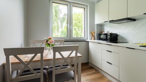 Et moderne køkken med hvide skabe, en mikrobølgeovn og et spiseområde med et træbord og stole.