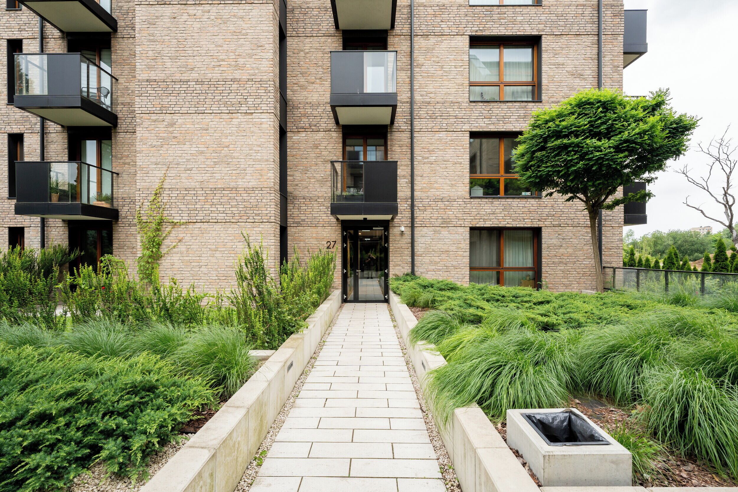 A multi-story building with a brick facade, balconies, and a pathway leading to the entrance.