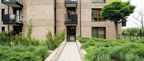 A multi-story building with a brick facade, balconies, and a pathway leading to the entrance.