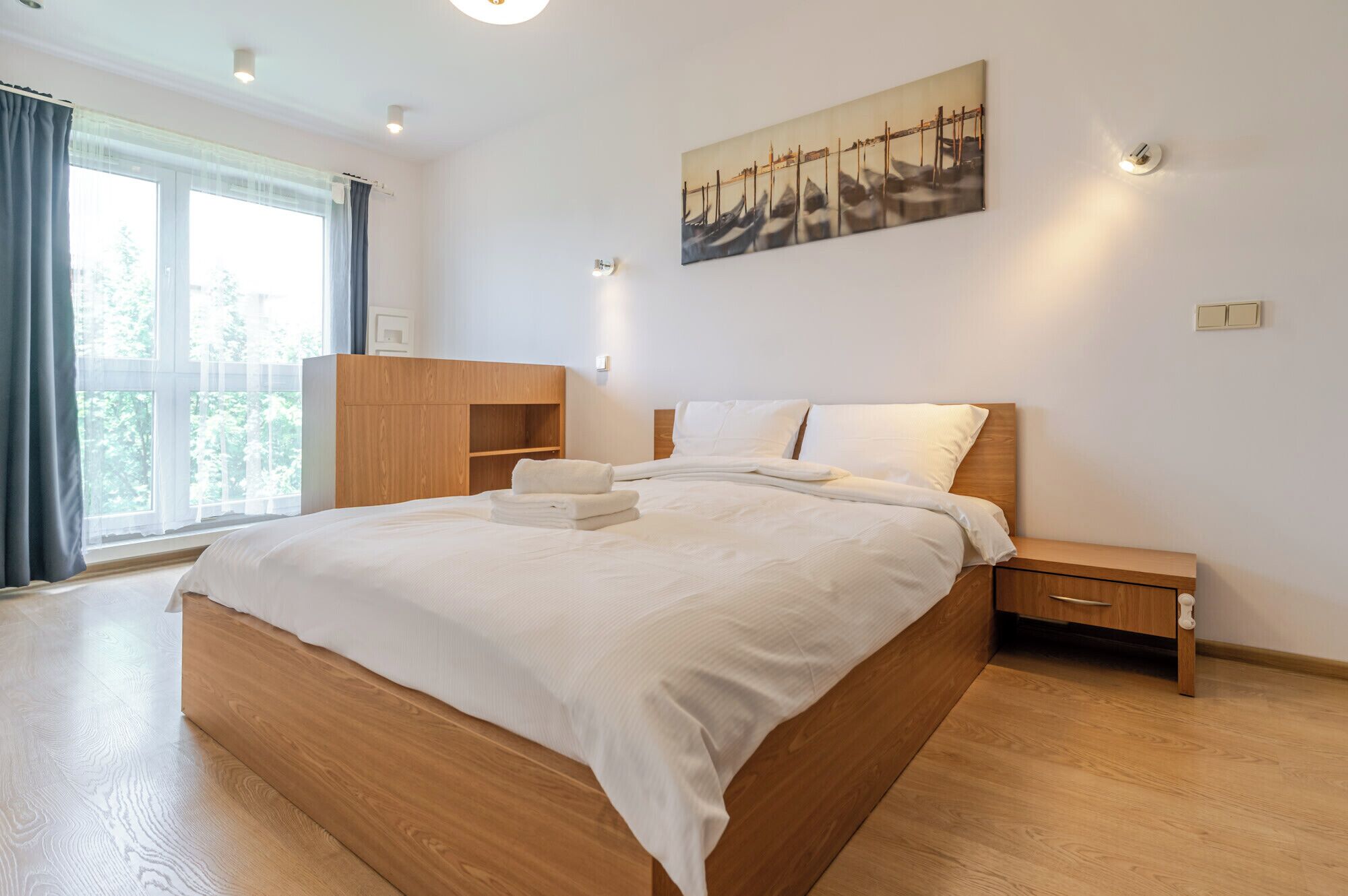 Una camera d'albergo moderna con un letto grande, un armadio in legno, un comodino, un quadro e una finestra con tende.
