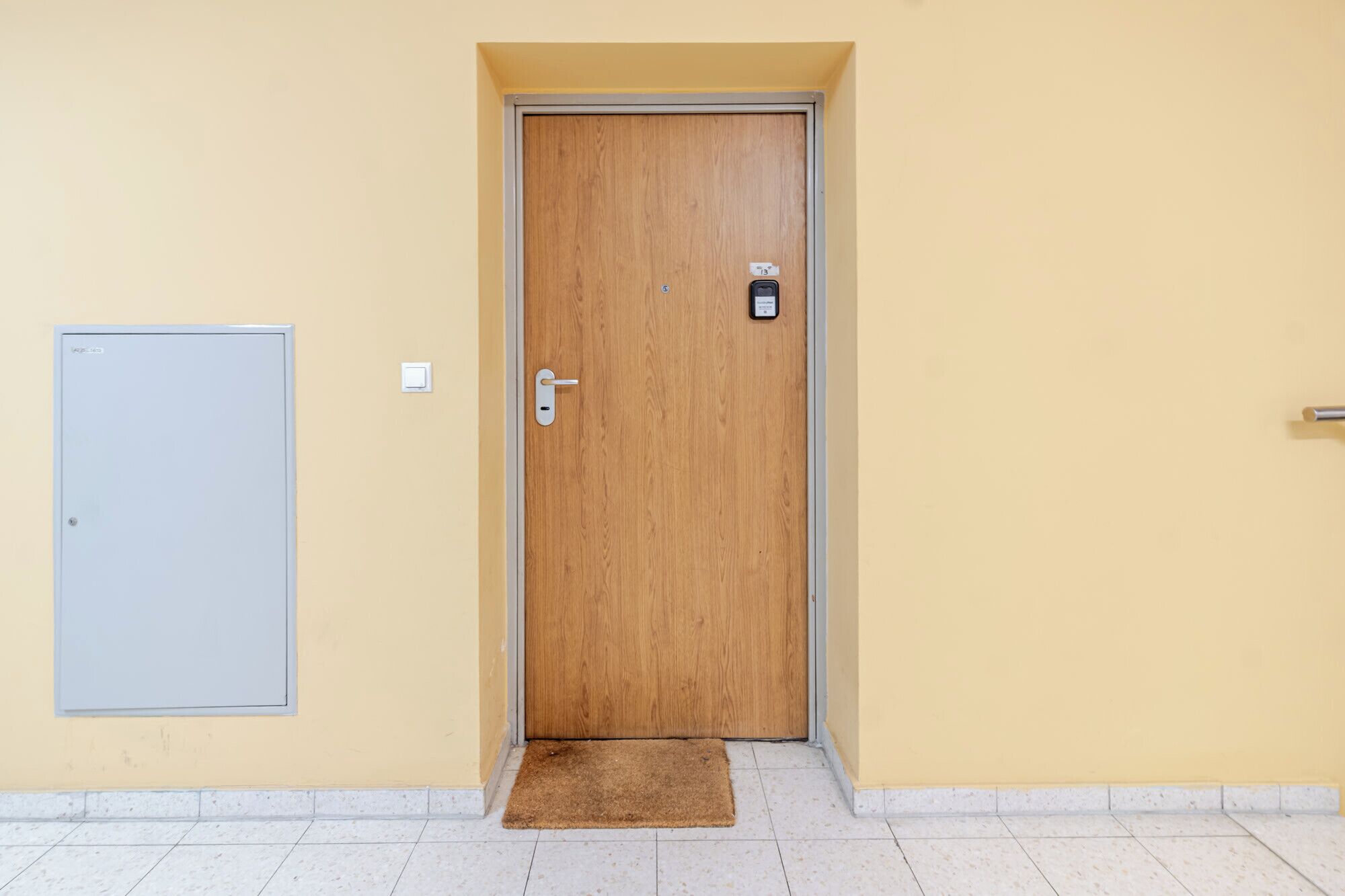 A wooden door with a keypad lock, a small mat at the entrance, and a light switch on the wall.