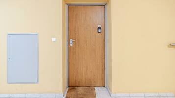 A wooden door with a keypad lock, a small mat at the entrance, and a light switch on the wall.