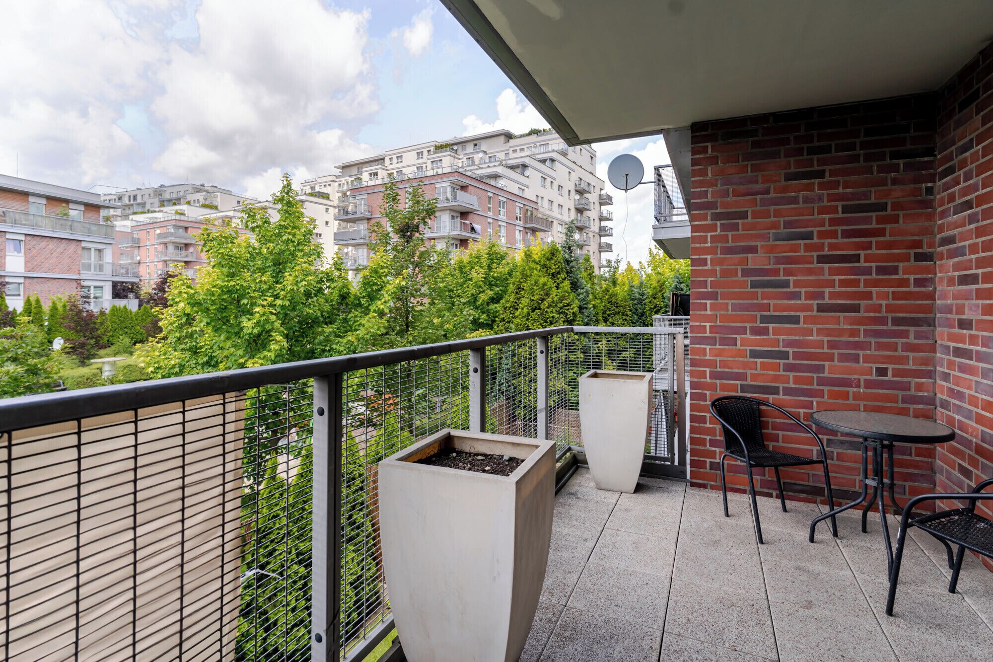 A balcony with a metal railing, two potted plants, and a table with two chairs.