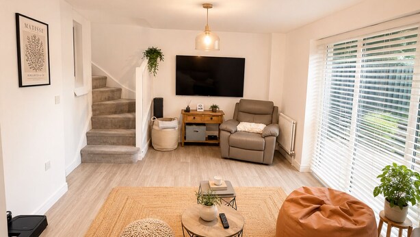 Una sala de estar con sofá, una mesa de centro, televisor, silla, escalera y ventana con persianas.
