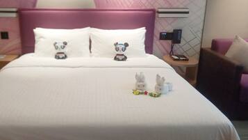 A hotel room with a bed, two pillows with panda designs, a nightstand with a phone, and a chair.