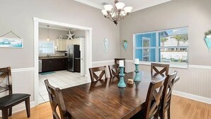 A dining room with a wooden table and chairs, a chandelier, and a view of the kitchen and outside through a window. - Sugar Sand 30A Retreat - 5BR Seagrove Home w/ Private Pool, 3 min walk to Beach! (Santa Rosa Beach)