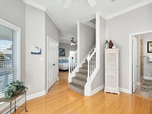 Un couloir doté d’un plancher en bois, de murs blancs, d’un escalier et d’une porte donnant sur une autre pièce.