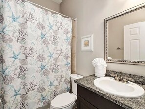 A bathroom with a shower curtain featuring a sea-themed pattern, a white toilet, a sink with a granite countertop, and a mirror with a decorative frame. - SugarSand30ARetreat-5BR Seagrove Home w/Private Heated Pool,3 min walk to Beach! (Santa Rosa Beach)
