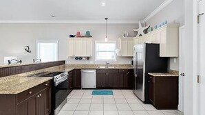 A modern kitchen with dark cabinetry, a stainless steel refrigerator, and a granite countertop. - Sugar Sand 30A Retreat - 5BR Seagrove Home w/ Private Pool, 3 min walk to Beach! (Santa Rosa Beach)