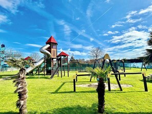 Ein Spielplatz mit Rutschen und Klettergerüsten, umgeben von Gras und Palmen.