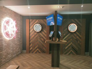 Een kamer met een dartbord, een neonbord en twee borden die 'Hat Tricks Sports Bar' adverteren.