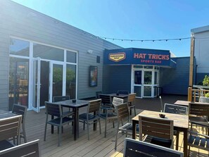 An outdoor seating area with tables and chairs, a sports bar sign, and a golf sign. - Holiday Park Home Sleeps 4 - Dogs Welcome - Pool (Clacton-on-Sea)