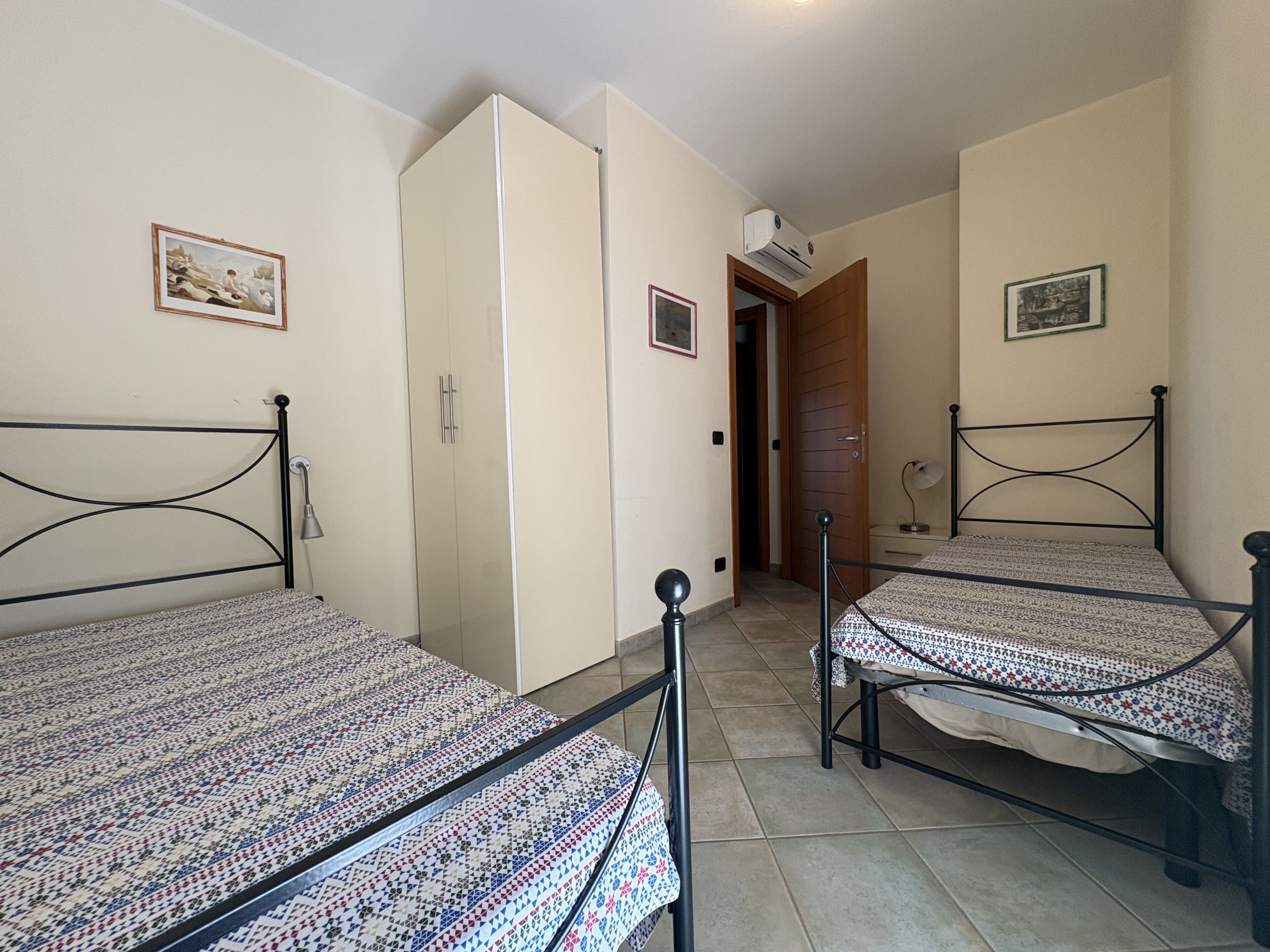 A room with two beds, a wardrobe, and a door leading to another room.