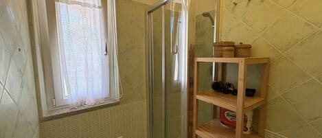 Ein Badezimmer mit Dusche, einem Fenster mit Vorhang und einem Holzregal mit Körben.