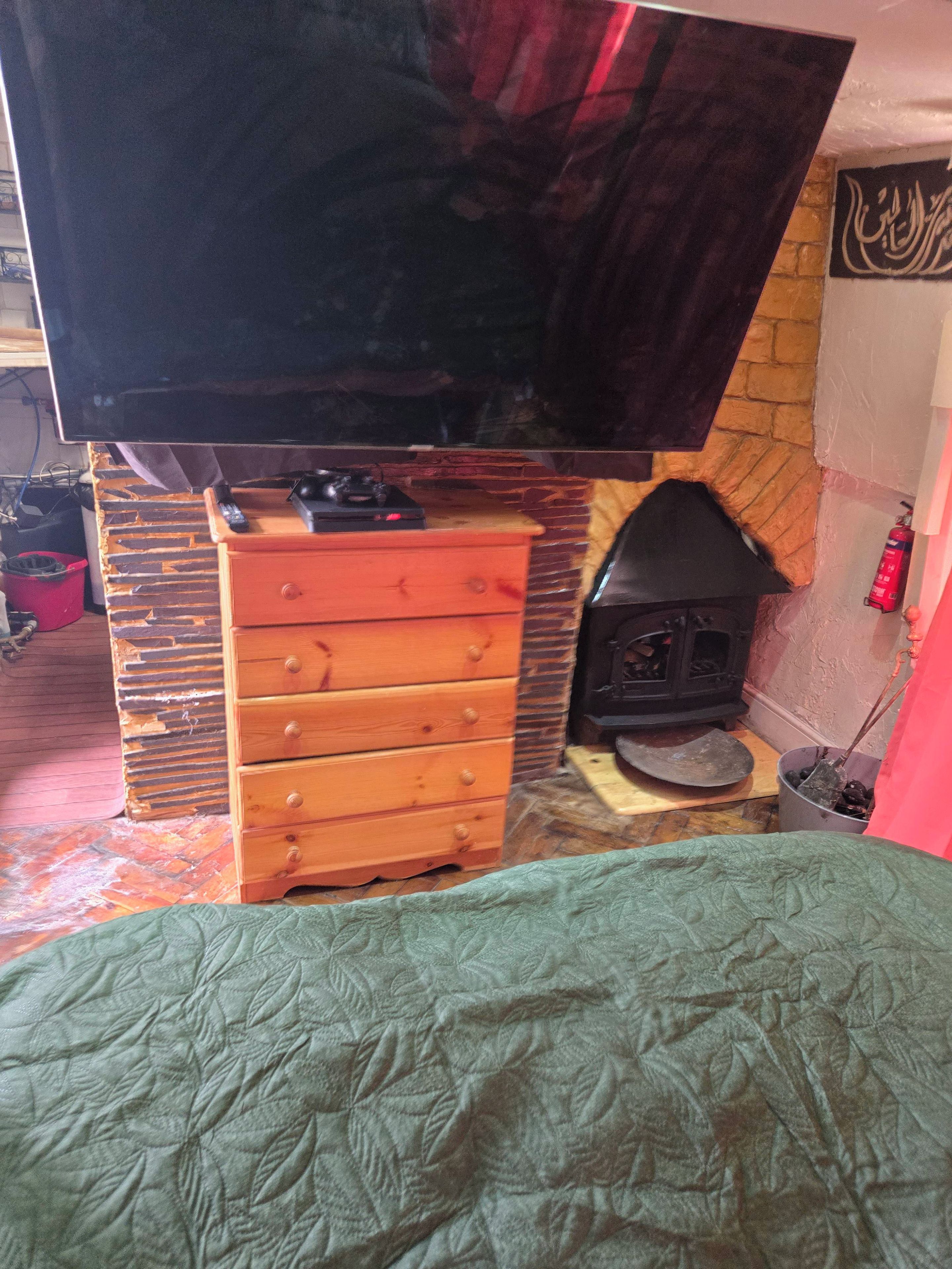 Ett rum med en öppen spis, en tv som hänger ovanför, och en byrå i trä.