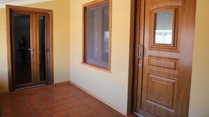 Ein Flur mit Fliesenboden, einer Holztür mit Fensterglas und einem Fenster mit Holzrahmen.