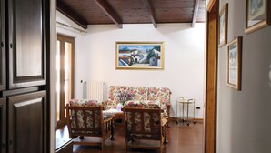 Ein Zimmer mit Holzbalkendecke, einem floralen Sofa, einem Esstisch mit Stühlen und einem Gemälde an der Wand.