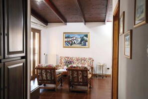 A room with a wooden ceiling, a floral sofa, a dining table with chairs, and a painting on the wall. - Sa Domu De Cadeddu - Three Bedroom Apartment, Sleeps 5 (Nurachi)