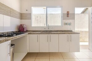 A kitchen with white cabinets, a gas stove, a window, and a decorative item on the wall. - House 50m from the beach with swimming pool (Itanhaém)