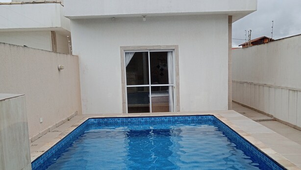 Une piscine rectangulaire bordée de carreaux, entourée d’un petit muret et d’un bâtiment blanc doté d’une fenêtre.