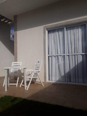 A patio area with a table and two chairs, a large window with curtains, and a wall-mounted picture. - House 50m from the beach with swimming pool (Itanhaém)