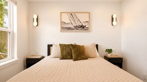 A bedroom with a large bed, two bedside tables, a wall-mounted light fixture, and a framed picture above the bed. - Spoonbill Cottage - New & Modern In Perfect Location w/ Waterfront Deck (St. Augustine)