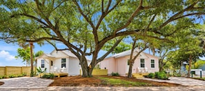 A two-story house with a large tree in front, a covered porch, and a small deck. - Spoonbill Cottage - New & Modern In Perfect Location w/ Waterfront Deck (St. Augustine)