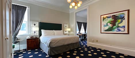 Habitación de hotel con cama, escritorio, silla, lámpara, un cuadro y alfombra estampada.