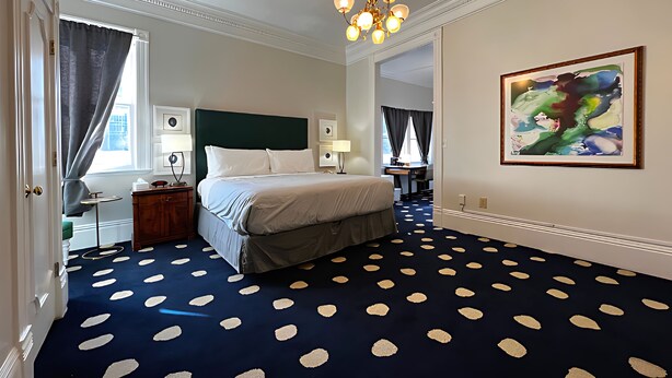 A hotel room with a bed, a desk, a chair, a lamp, a painting, and a patterned carpet. - Stylish Deluxe King Retreat in the Heart of Sacramento (Sacramento)