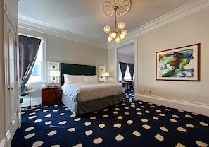 Quarto de hotel com cama, escrivaninha, cadeira, luminária, quadro e tapete estampado.