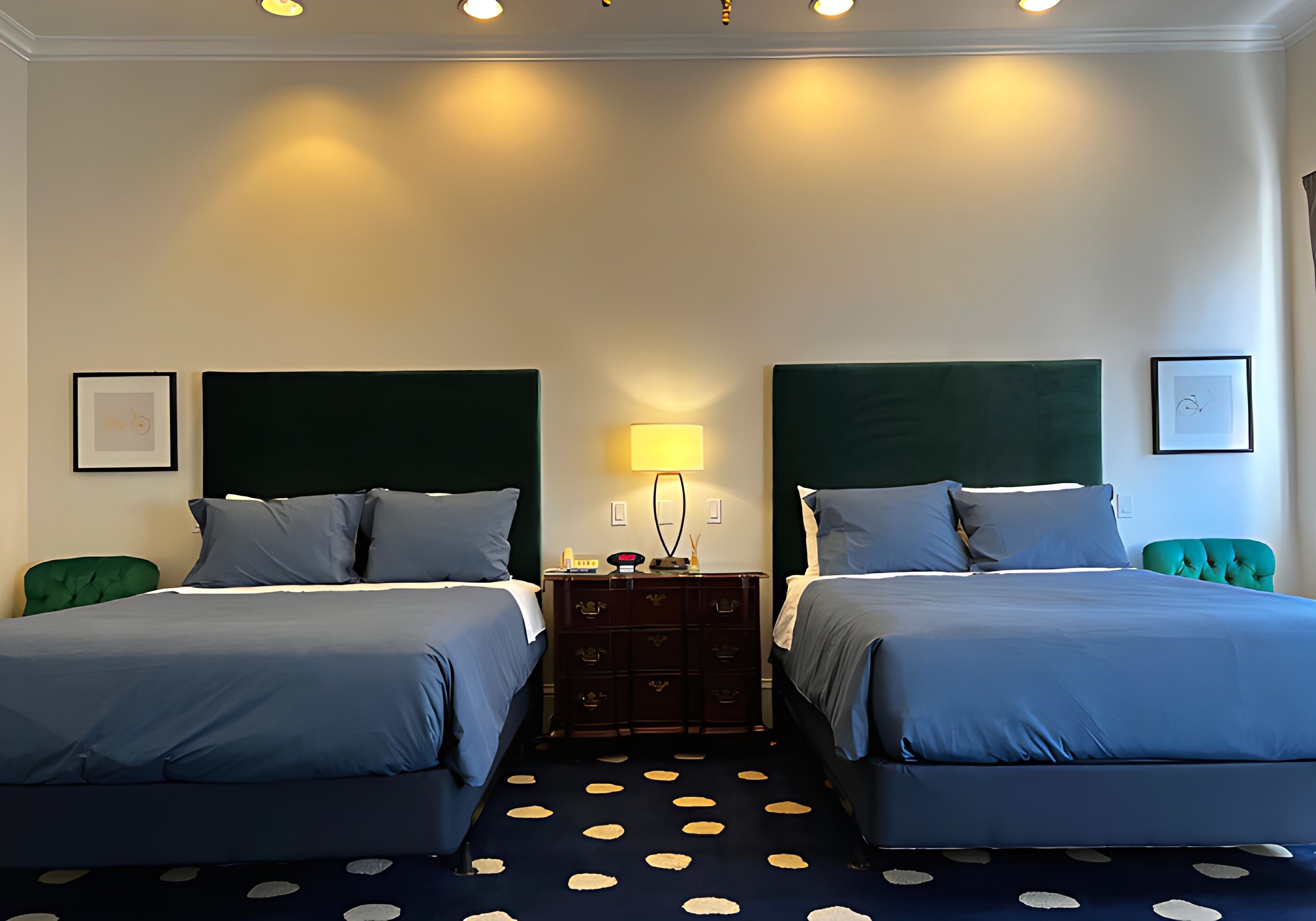 Habitación de hotel con dos camas, un aparador, una lámpara y una alfombra de lunares.