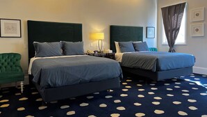 Et hotelværelse med to senge, en grøn lænestol, et mønstret tæppe og et vindue med gardiner.