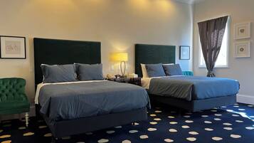 Habitación de hotel con dos camas, un sillón verde, alfombra estampada y una ventana con cortinas.