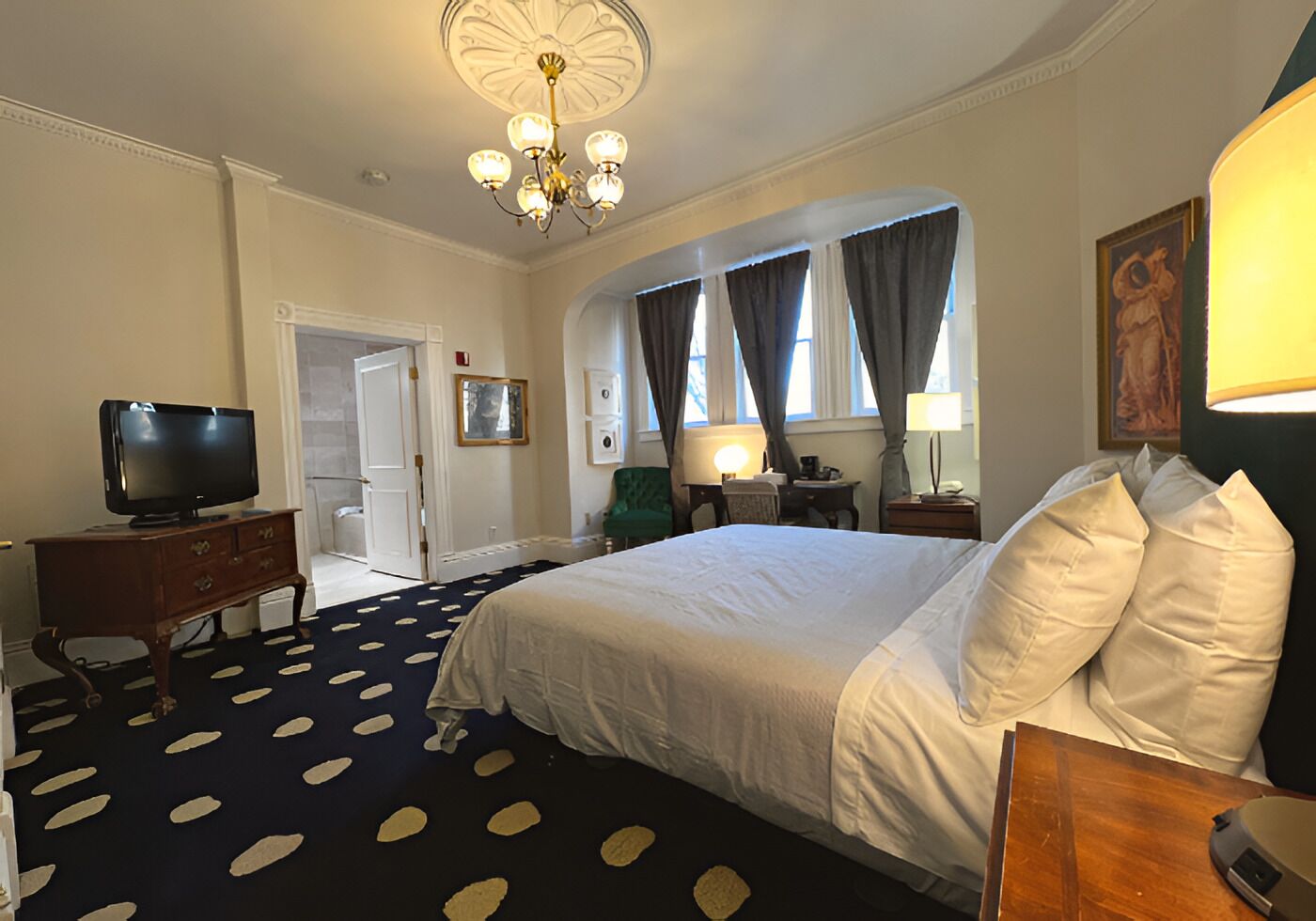 Ein Hotelzimmer mit einem großen Bett, einem Fernseher, einem Schreibtisch mit Lampe und einem Kronleuchter.