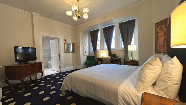 Habitación de hotel con una cama grande, televisor, escritorio con lámpara y candelabro.