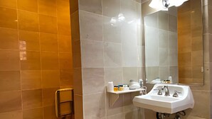 Un baño con lavamanos blanco, espejo y repisa con artículos de tocador.
