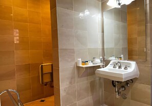 Un baño con lavamanos blanco, espejo y repisa con artículos de tocador.