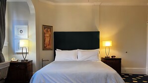 Habitación de hotel con una cama grande, dos mesitas de noche con lámparas, un cuadro en la pared y una alfombra estampada.