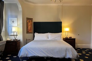 Habitación de hotel con una cama grande, dos mesitas de noche con lámparas, un cuadro en la pared y una alfombra estampada.