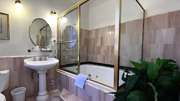 Un baño con lavamanos pedestal, bañera, espejo grande y planta en maceta.