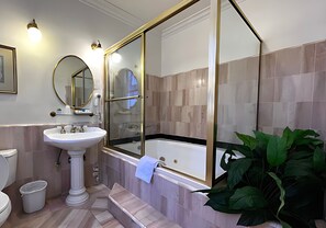 Un baño con lavamanos pedestal, bañera, espejo grande y planta en maceta.
