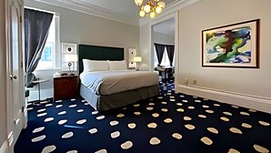 Hotelkamer met een bed, een bureau, een stoel, een bureaulamp, een kunstwerk aan de wand en een kamerbreed tapijt met dessin.