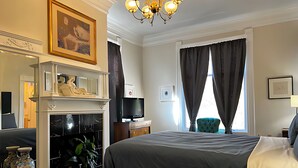Een hotelkamer met een bed, een televisie, een open haard, een spiegel en een raam met gordijnen.