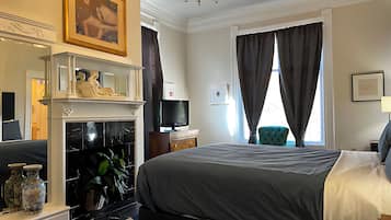 Una habitación de hotel con cama, televisión, chimenea, espejo y ventana con cortinas.