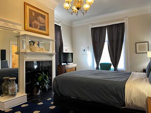 Una habitación de hotel con cama, televisión, chimenea, espejo y ventana con cortinas.