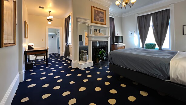 Een hotelkamer met een bed, een open haard, een bureau en een groot raam met gordijnen.