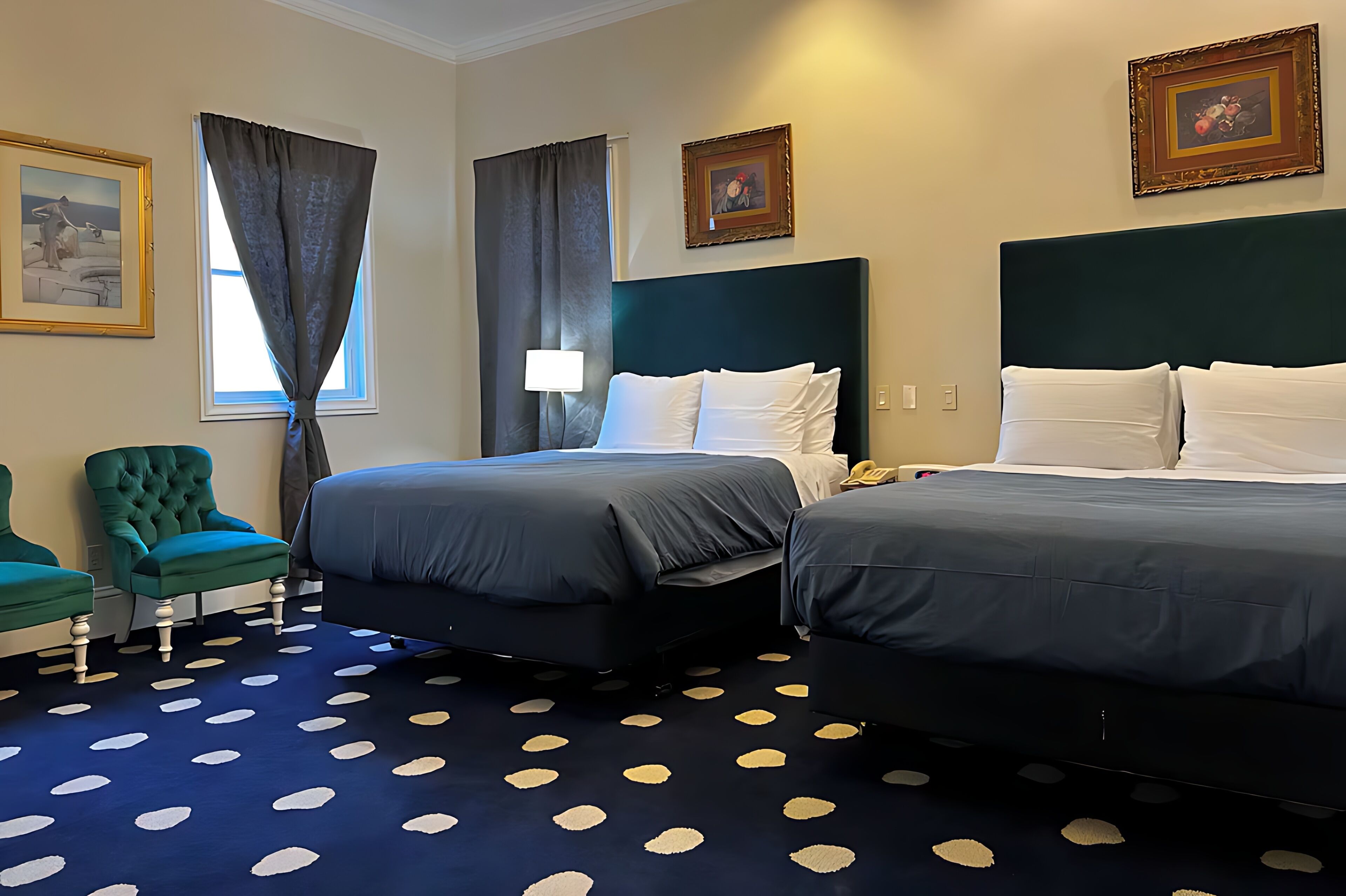 Quarto de hotel com duas camas, uma poltrona verde, carpete estampado e obras de arte emolduradas nas paredes.