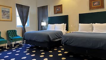 Una habitación de hotel con dos camas, un sillón verde, alfombra estampada y cuadros en las paredes.