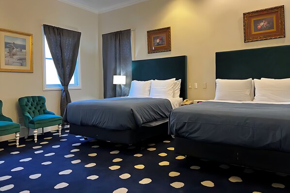 Una habitació d'hotel amb dos llits, un butacó verd, una catifes amb dibuixos i quadres a les parets.